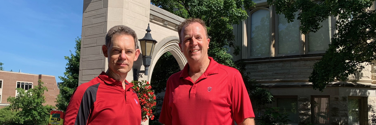 Greg Siering and Randy Newbrough, both in red shirts, standing at Indiana University's Sample Gates