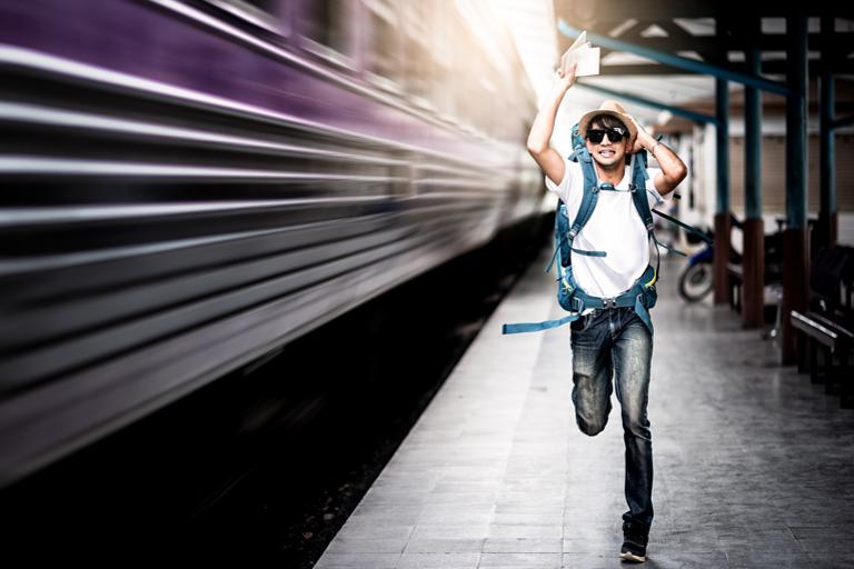 man with backpack running on a train platform after a moving train