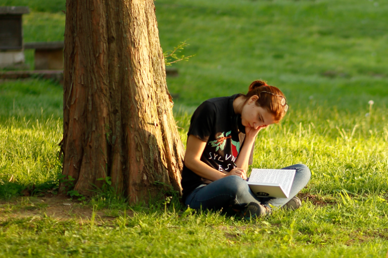 College woman reading a book at the base of a tree